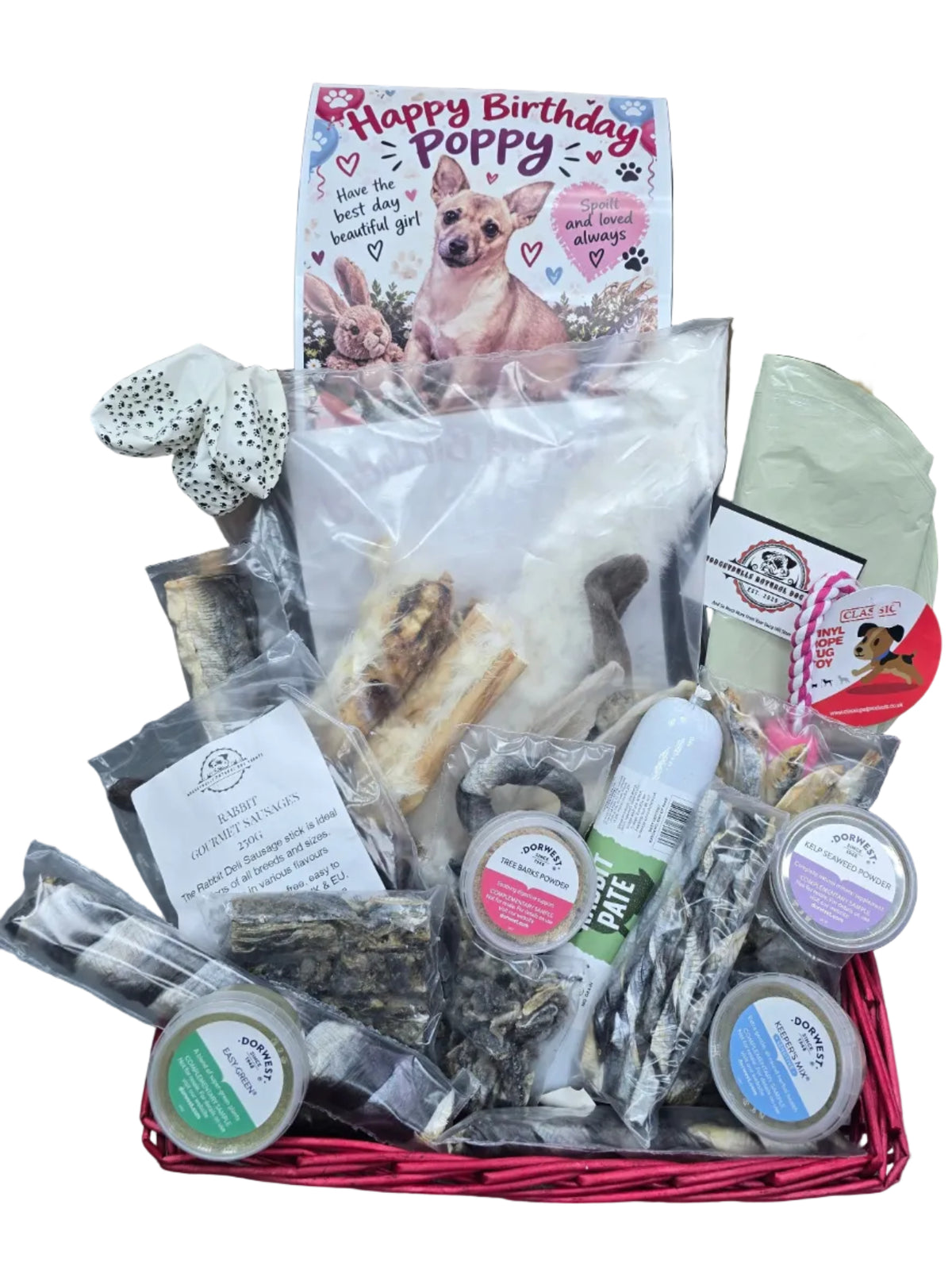 A dog treat gift basket filled with various dog treats, chews, and packaged snacks, including a 'Happy Birthday Poppy' card, set against a rustic wooden background.